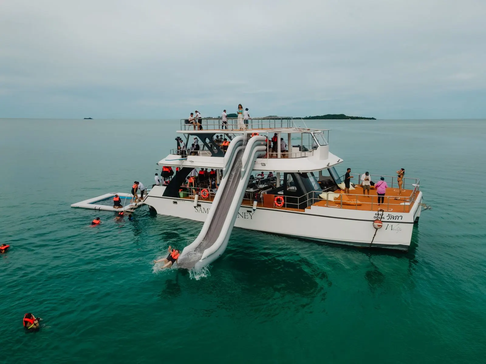 Der Katamaran von Samui Journey vor Anker, mit Wasserrutsche und schwimmendem Meerespool, Gäste schwimmen daneben