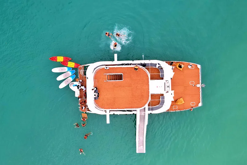 Top-down drone view of the catamaran with kayaks, paddleboards and the slide, guests swimming alongside