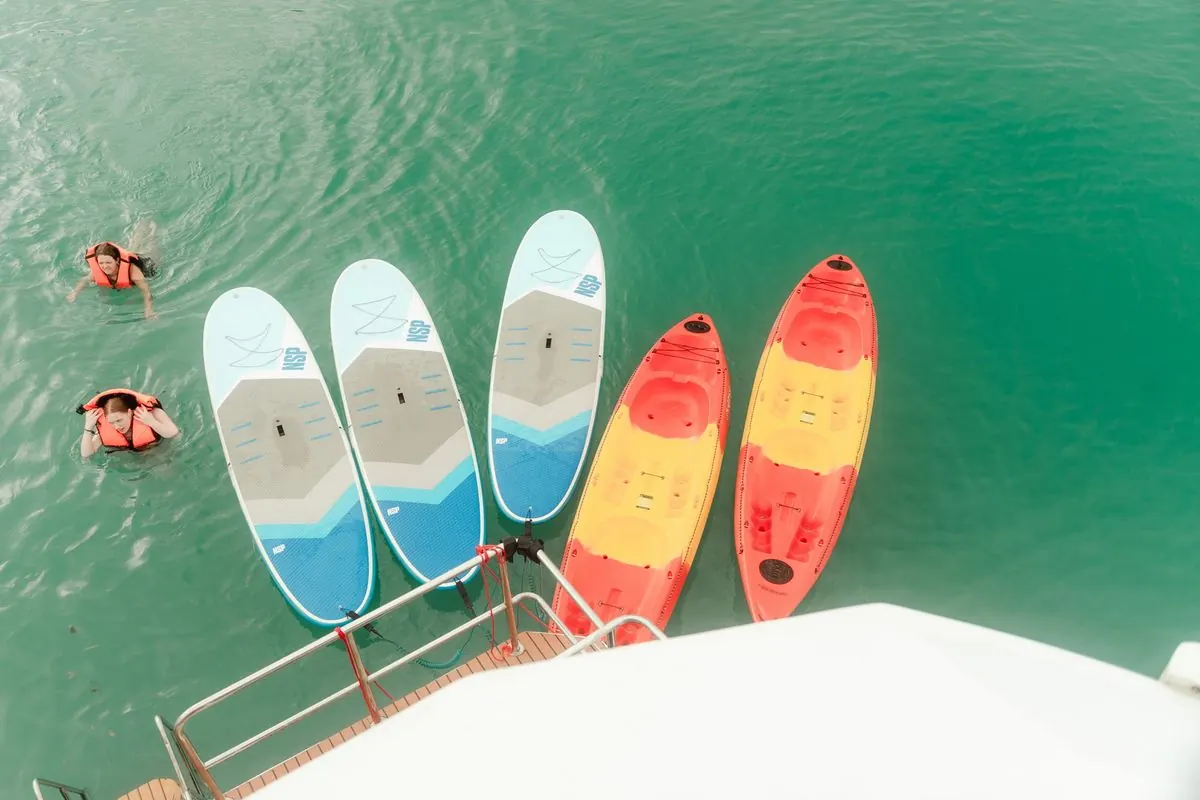 Stand-up-Paddle-Boards und Kajaks neben dem Katamaran, vom Deck aus gesehen