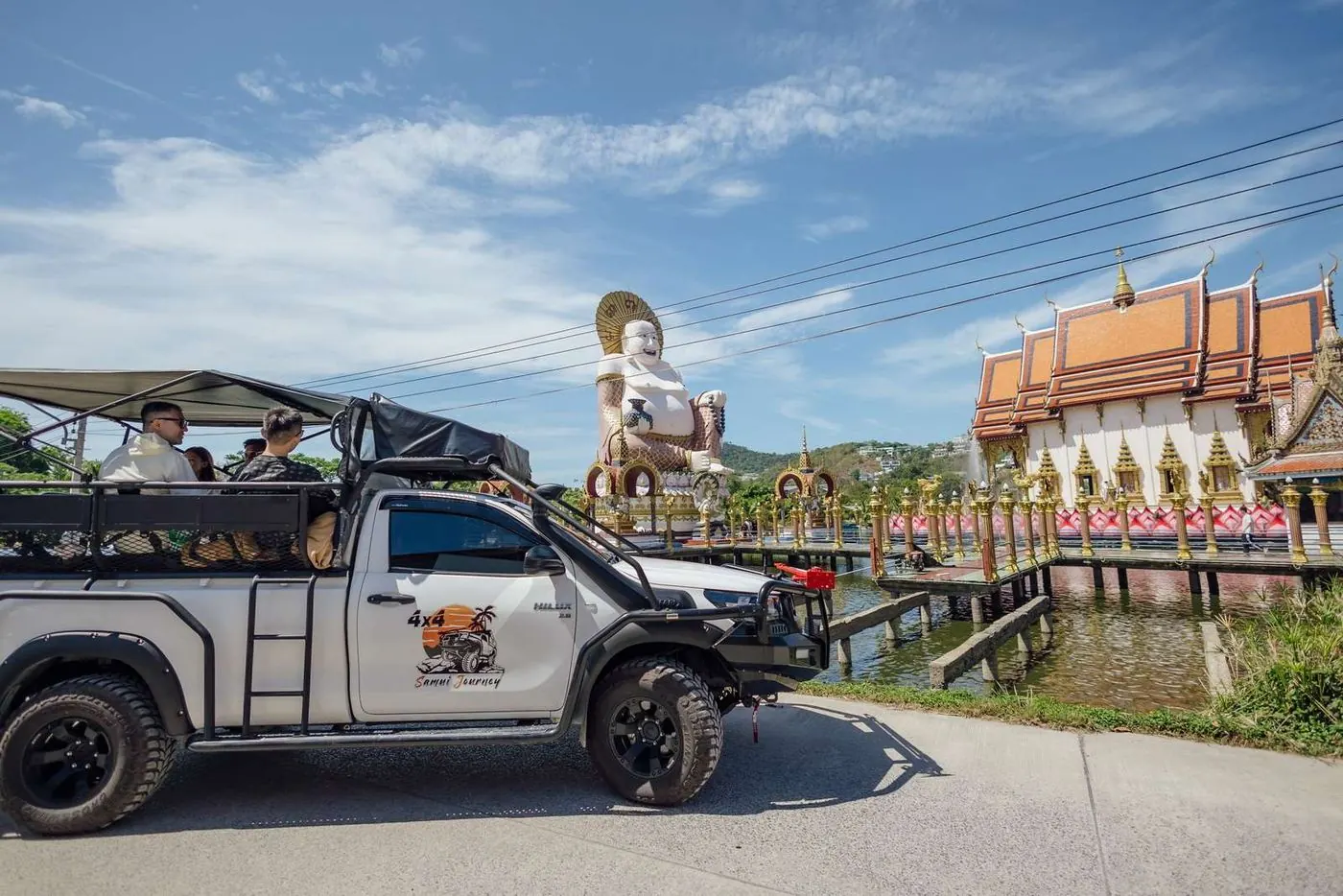 The 4x4 safari truck beside a lakeside Koh Samui temple with a large laughing Buddha statue