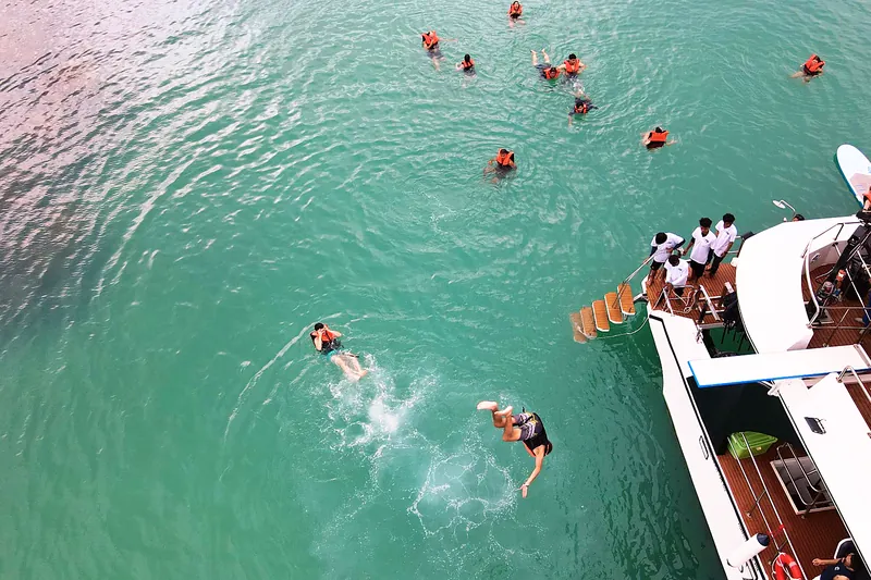 Guests jumping from the catamaran into the sea while others swim in life jackets