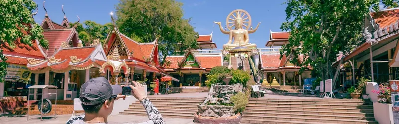 A visitor photographing a golden Buddha statue at a temple, one of the quieter things to do in south Koh Samui