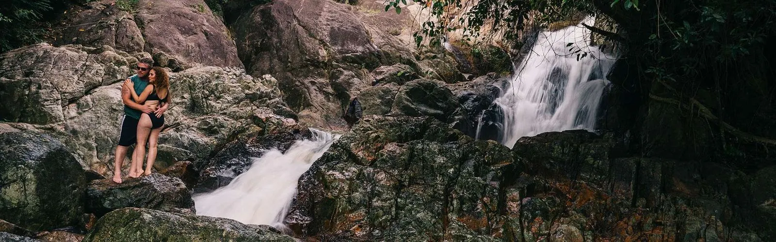 A couple posing on the rocks beside a jungle waterfall on Koh Samui